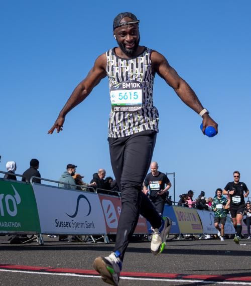 Man with arms outstretched smiling as he crosses the finish line at brighton 10k