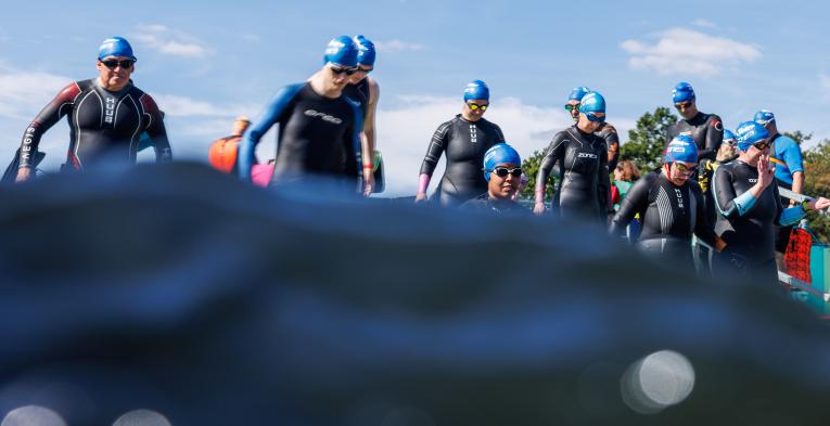 Water covers the bottom half of the image, above the waterline you can see a group of swimmers in wetsuits and googles waiting to start the Swim Serpentine event
