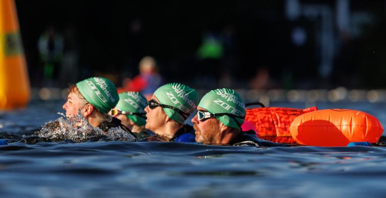 Group of swimmers in green caps swim in the serpentine.