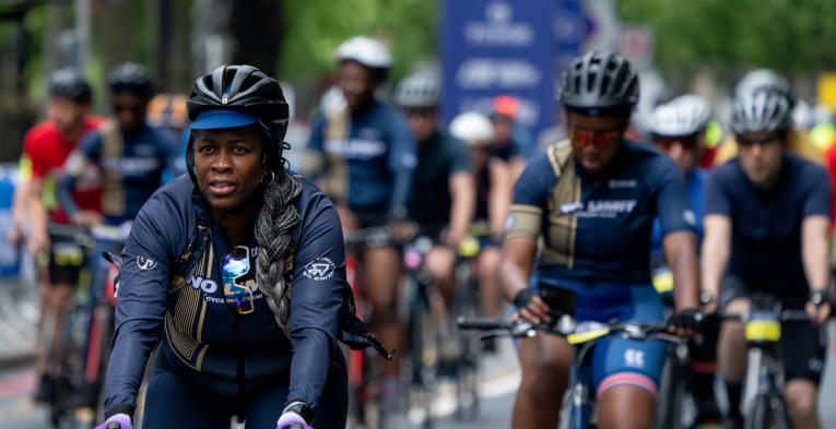 Woman cycling on a road looking into the distance with other cyclists in the background.