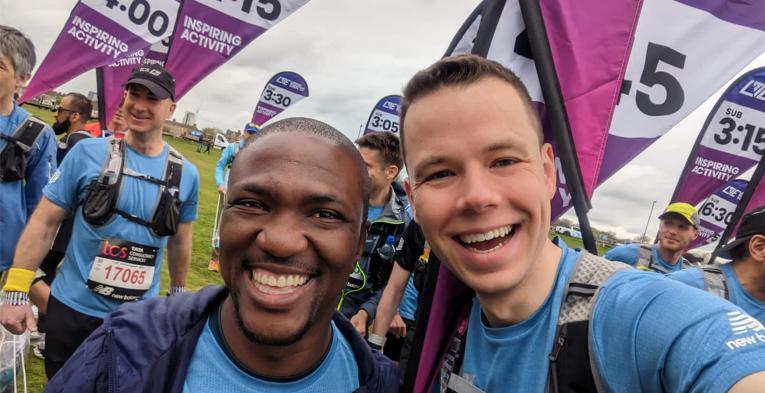 A selfie of two guys. One runner and one pace team member, with multiple pace team members behind them. 