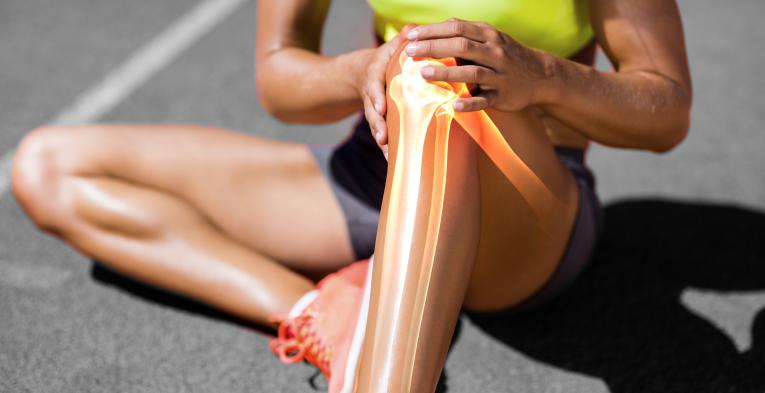 Runner suffering from knee pain while sitting on track during a sunny day
