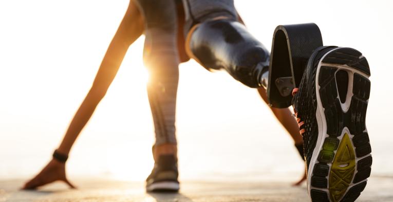 Back view of disabled athlete woman with prosthetic leg getting ready to run outdoors