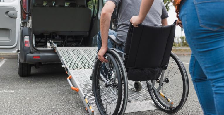 Someone pushing a wheelchair user up a rump into a vehicle