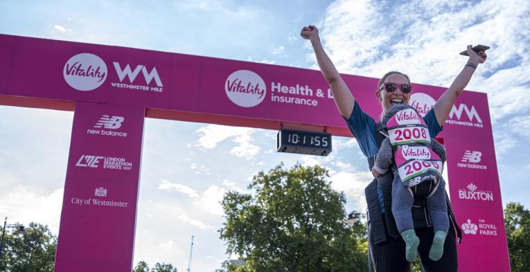 Woman with her child at the Finish throws her arms in the air 