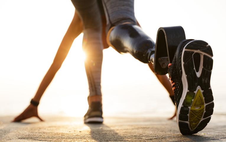Back view of disabled athlete woman with prosthetic leg getting ready to run outdoors