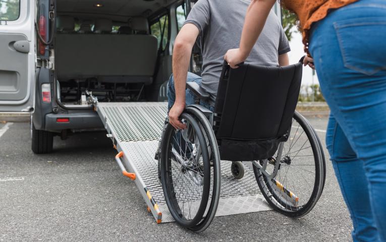 Someone pushing a wheelchair user up a rump into a vehicle