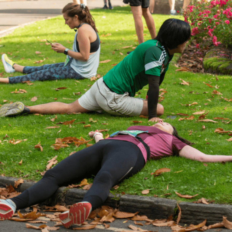 People lying down and stretching on the grass after running.