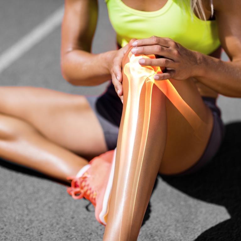 Runner suffering from knee pain while sitting on track during a sunny day