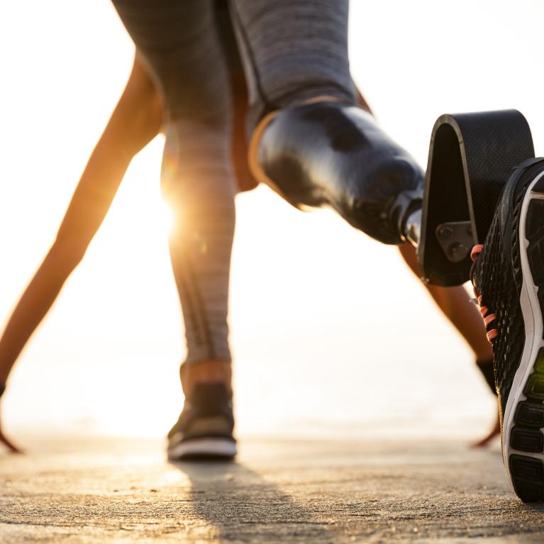 Back view of disabled athlete woman with prosthetic leg getting ready to run outdoors