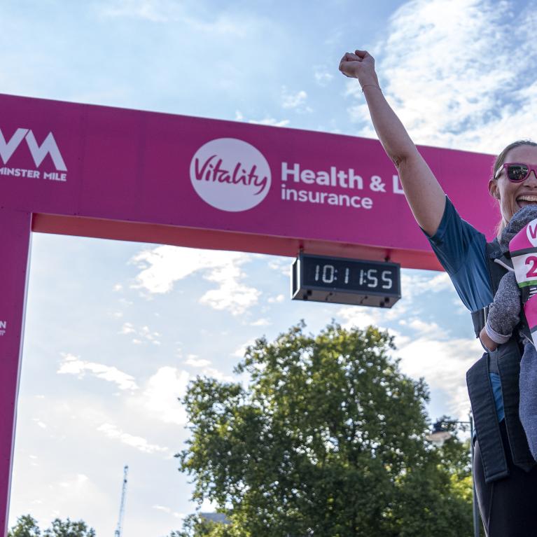 Woman with her child at the Finish throws her arms in the air 