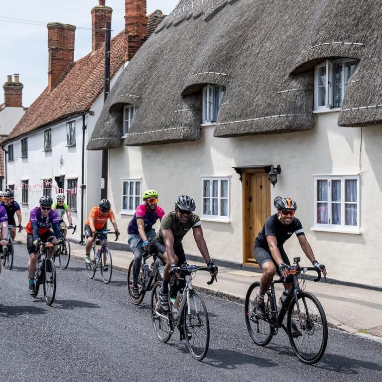 Cyclists ride past a thatched cottage