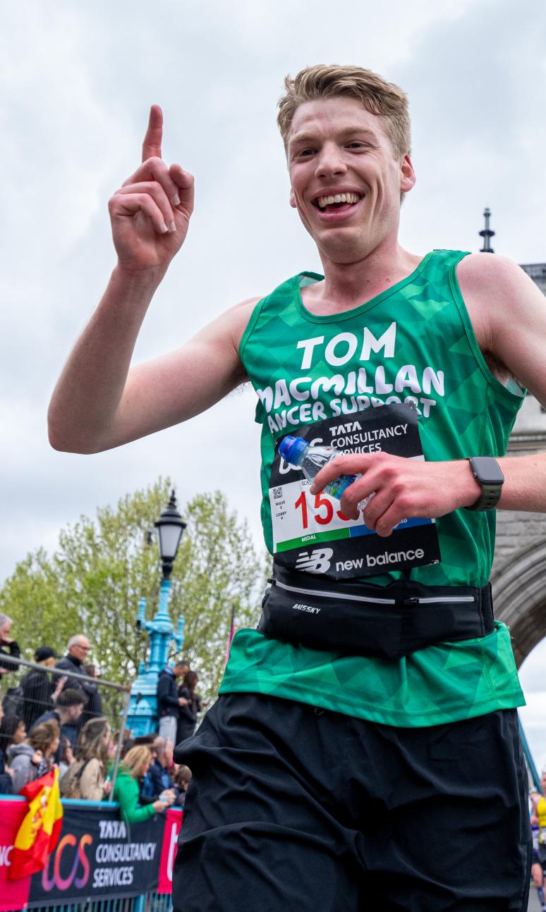 Runner in a green vest with a finger in the air celebrating. Tower bridge in the background.