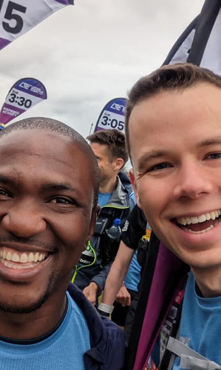 A selfie of two guys. One runner and one pace team member, with multiple pace team members behind them. 