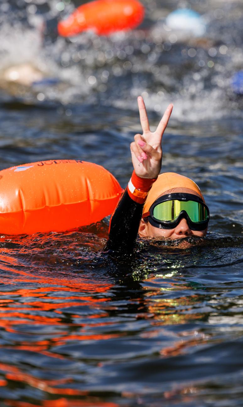 Swim Serpentine participant holds up a peace sign from the water