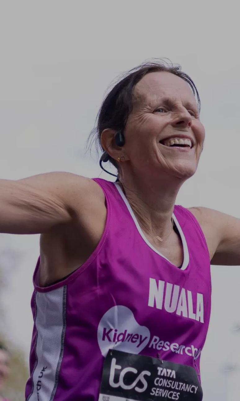 A runner with her arms out stretched in a charity running vest as she crosses the Finish Line