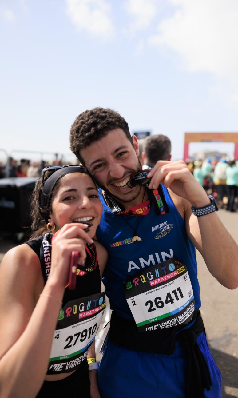 couple bite down on their medals at the Brighton Marathon finish