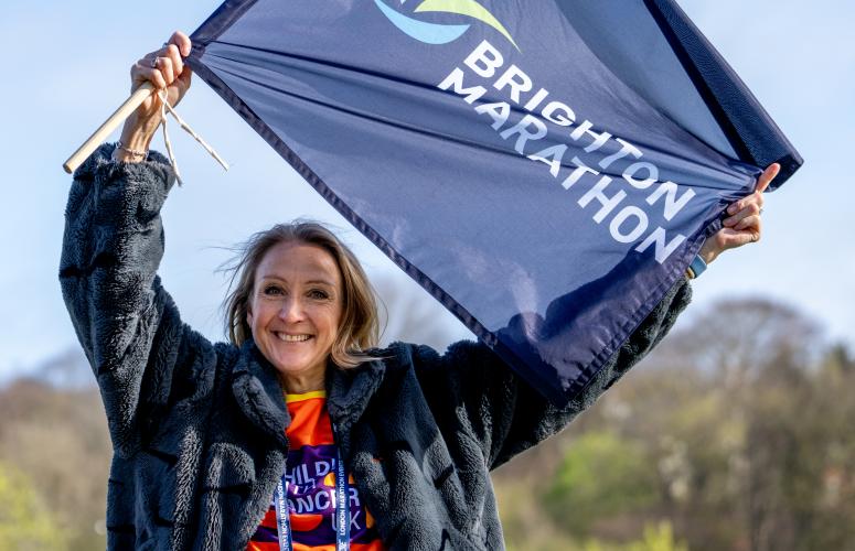 Woman stands with trees in the background holding a Brighton marathon flag