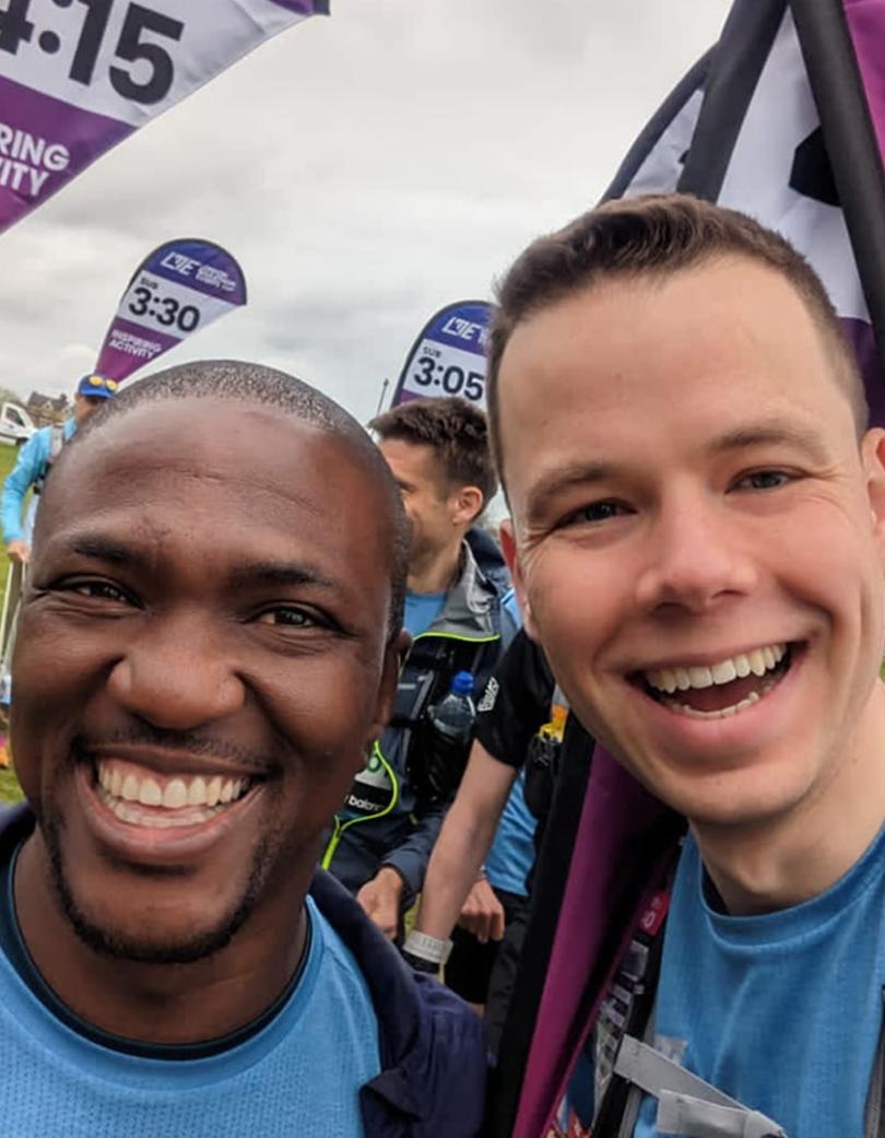 A selfie of two guys. One runner and one pace team member, with multiple pace team members behind them.