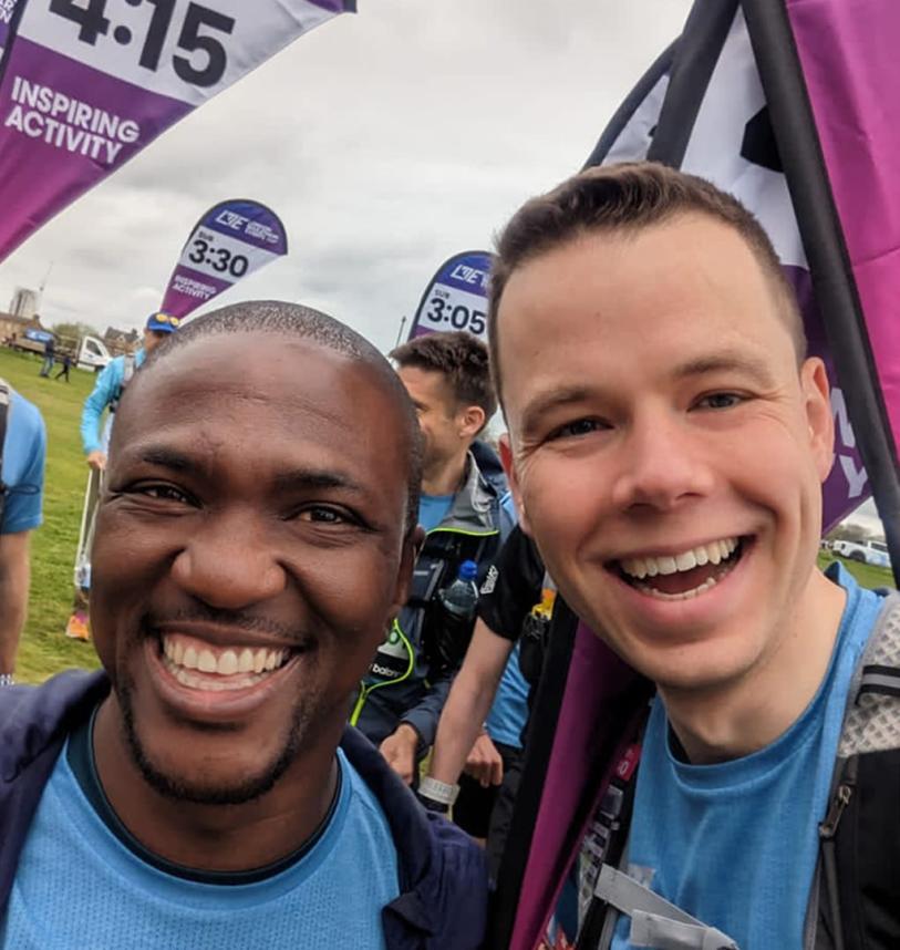 A selfie of two guys. One runner and one pace team member, with multiple pace team members behind them.