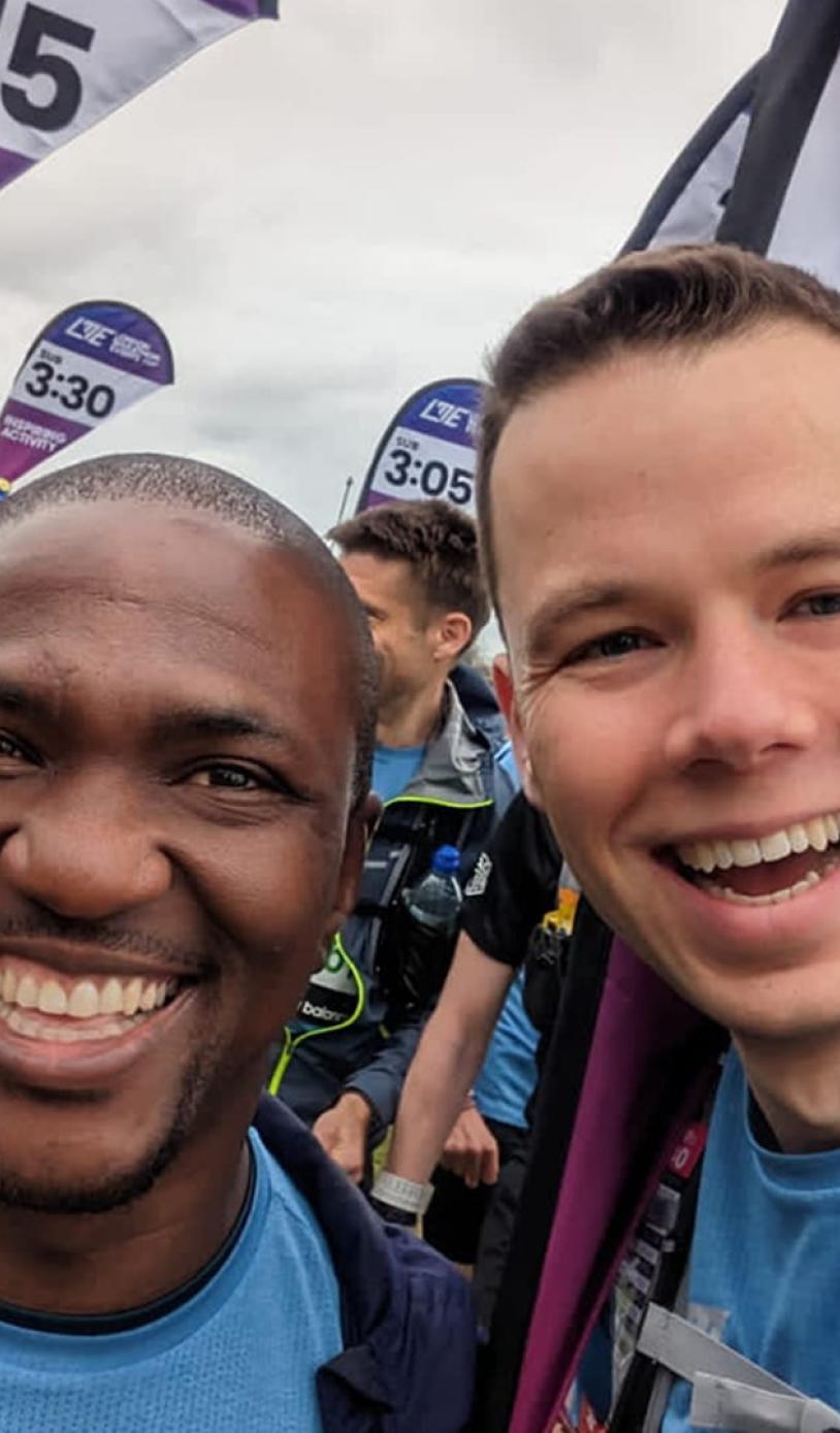 A selfie of two guys. One runner and one pace team member, with multiple pace team members behind them. 