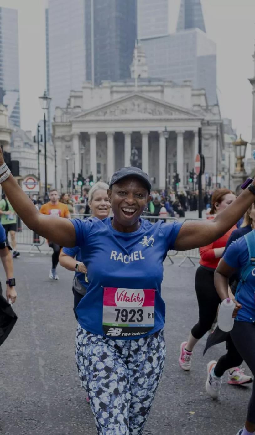 A runner with her arms out stretched in a charity running vest as she runs through London